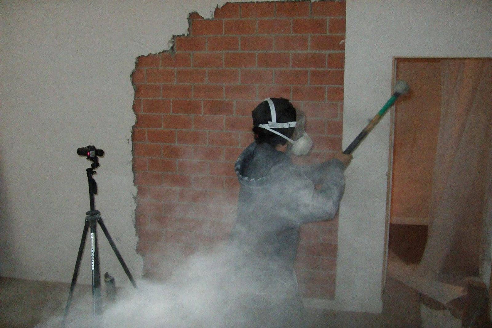 Werkman met stofmasker en veiligheidsbril breekt een niet-dragende binnenmuur af met een voorhamer