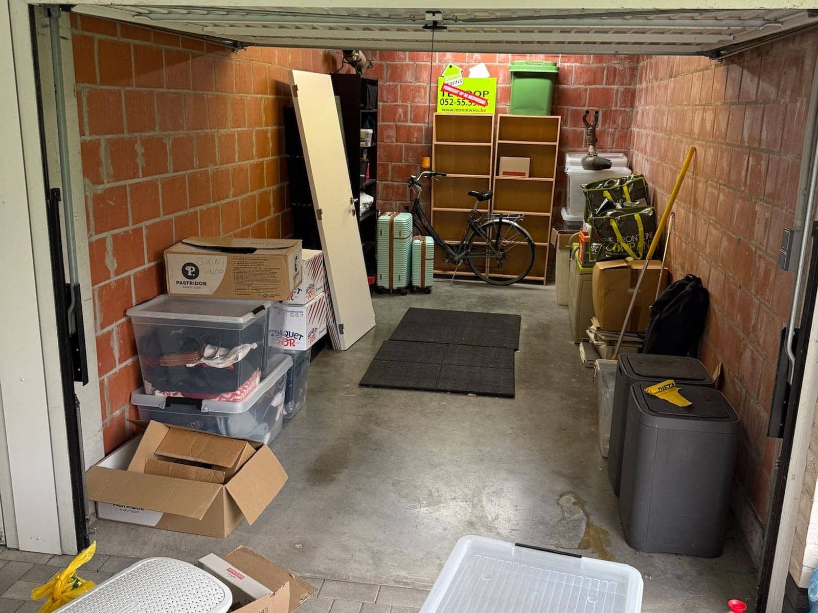 Garage vol dozen, plastic bakken en vuilnisbakken, met spullen tot op de oprit