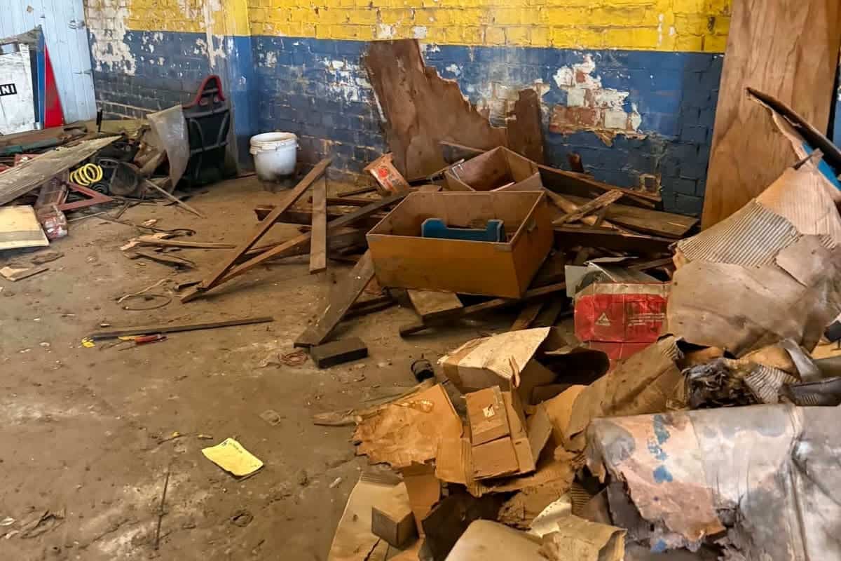 Berg hout, karton en oude rommel opgestapeld tegen de muur van een loods, klaar om afgevoerd te worden