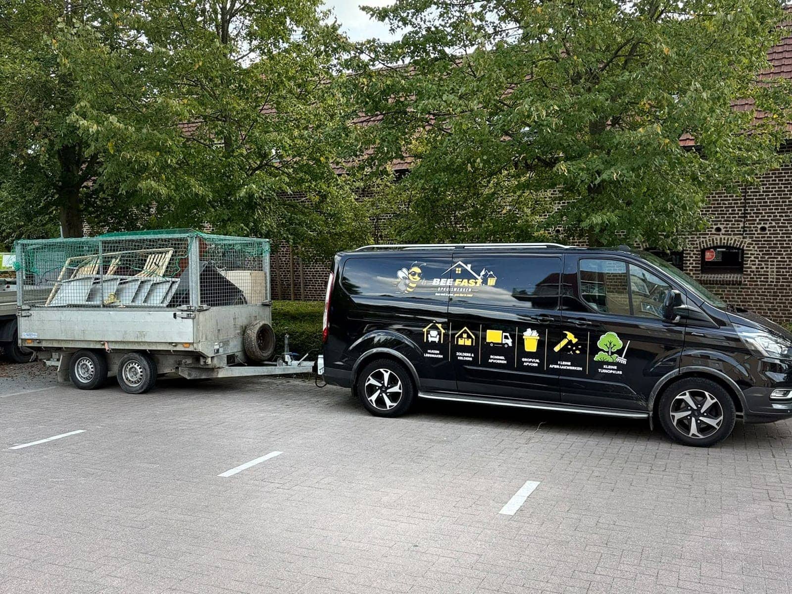 De bestelwagen van Bee Fast met de volgeladen aanhangwagen erachter op een parking