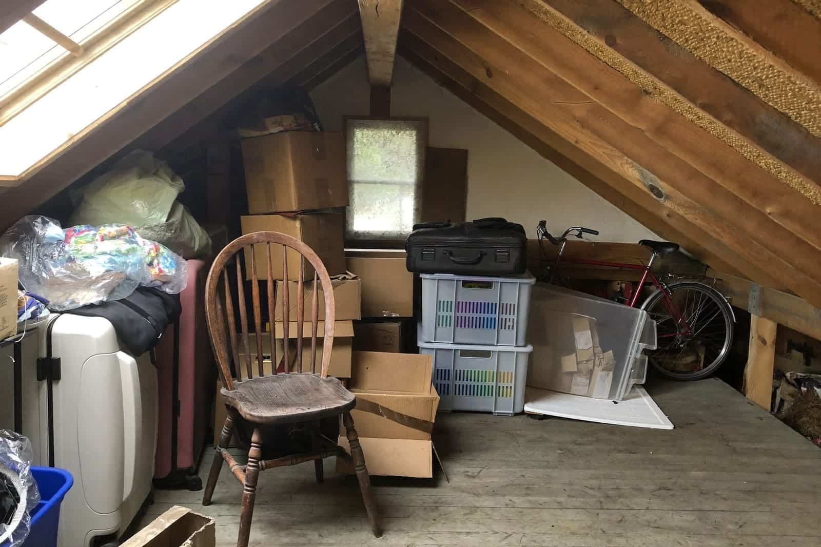 Volle zolder onder houten dakspanten met dozen, koffers en oude spullen die opgeruimd moeten worden